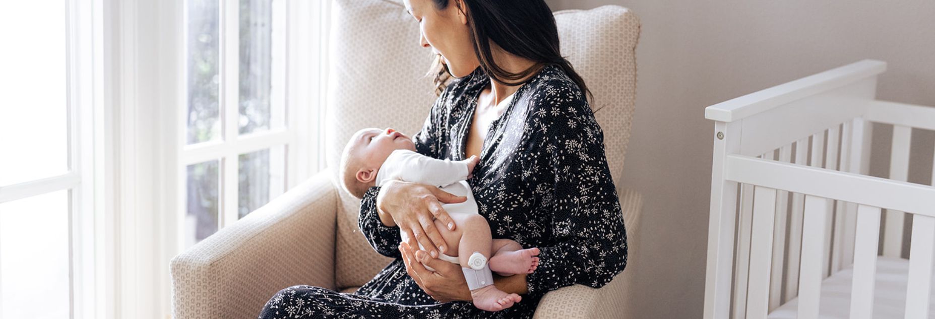 Mother holding her baby near a crib, using the Hälsa Baby monitor to create a soothing, comfortable environment.